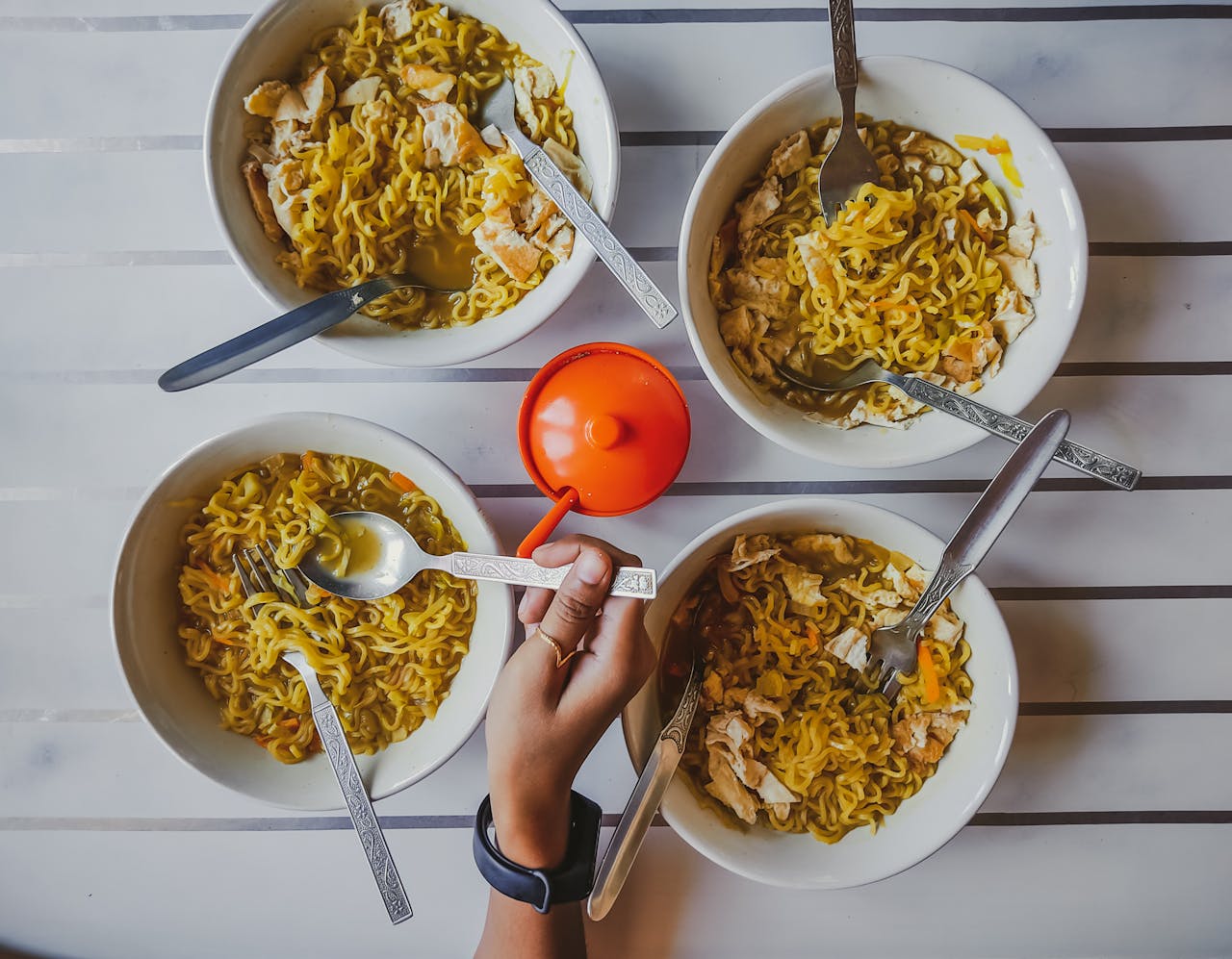 ours-journey An overhead shot featuring multiple bowls of noodles with a hand reaching in, showcasing a communal meal.