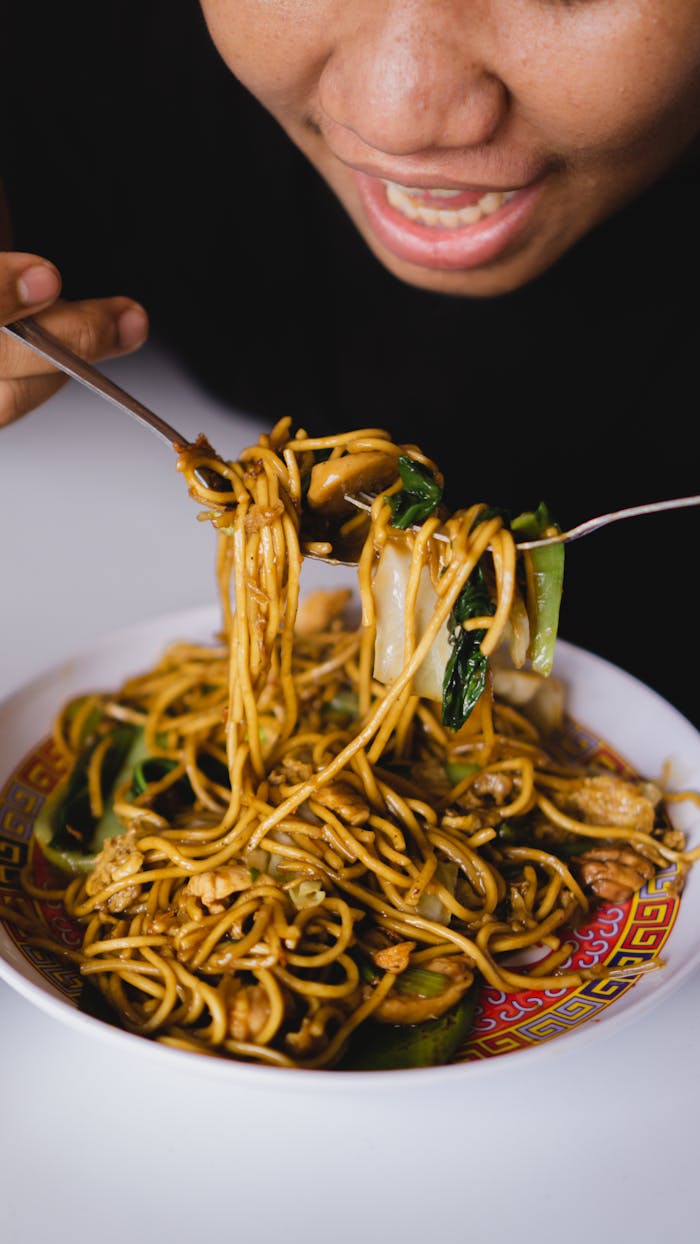 Close-up of a person enjoying a traditional Indonesian noodle dish indoors. Vibrant and appetizing.
