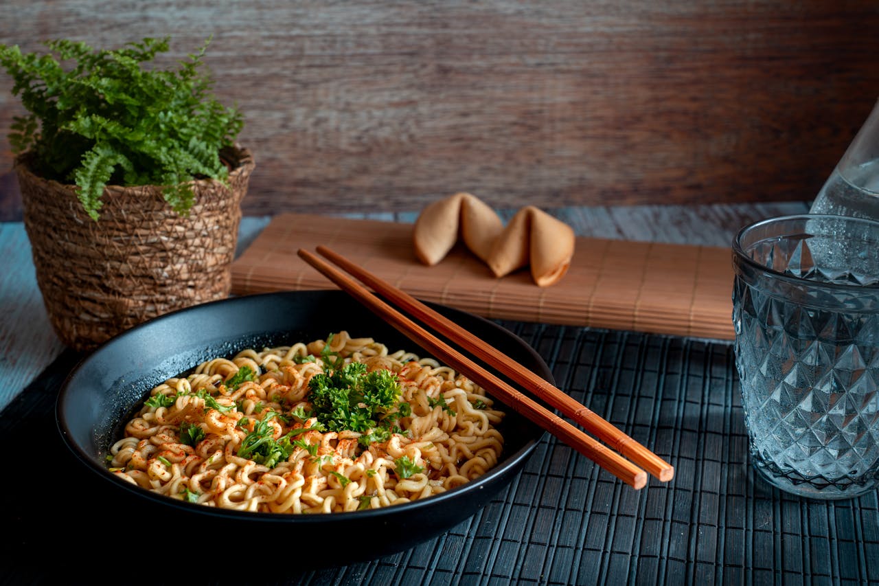A savory noodle dish garnished with herbs, paired with chopsticks and fortune cookies.