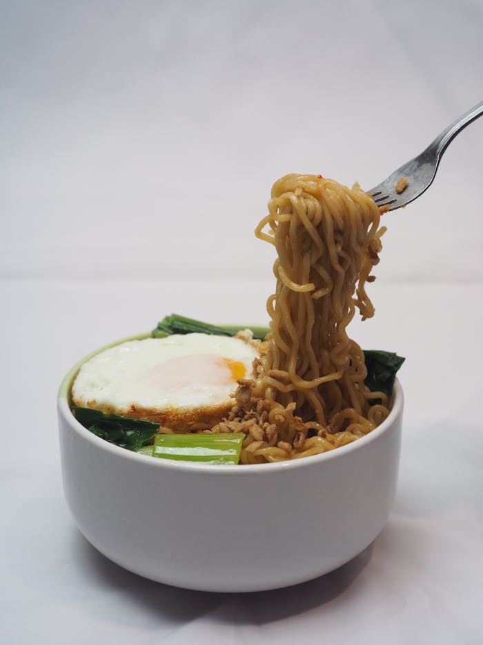 Indonesian noodle bowl with fried egg and vegetables in a white bowl on a white background.