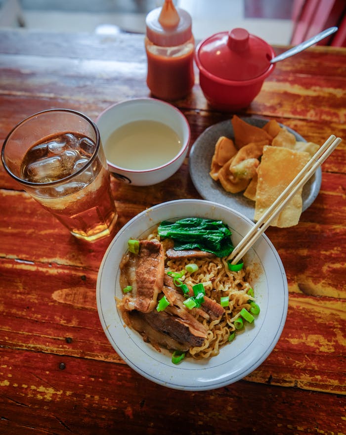 Delicious Indonesian beef noodle dish with fresh vegetables, crispy snacks, and dipping sauce served in Jakarta.