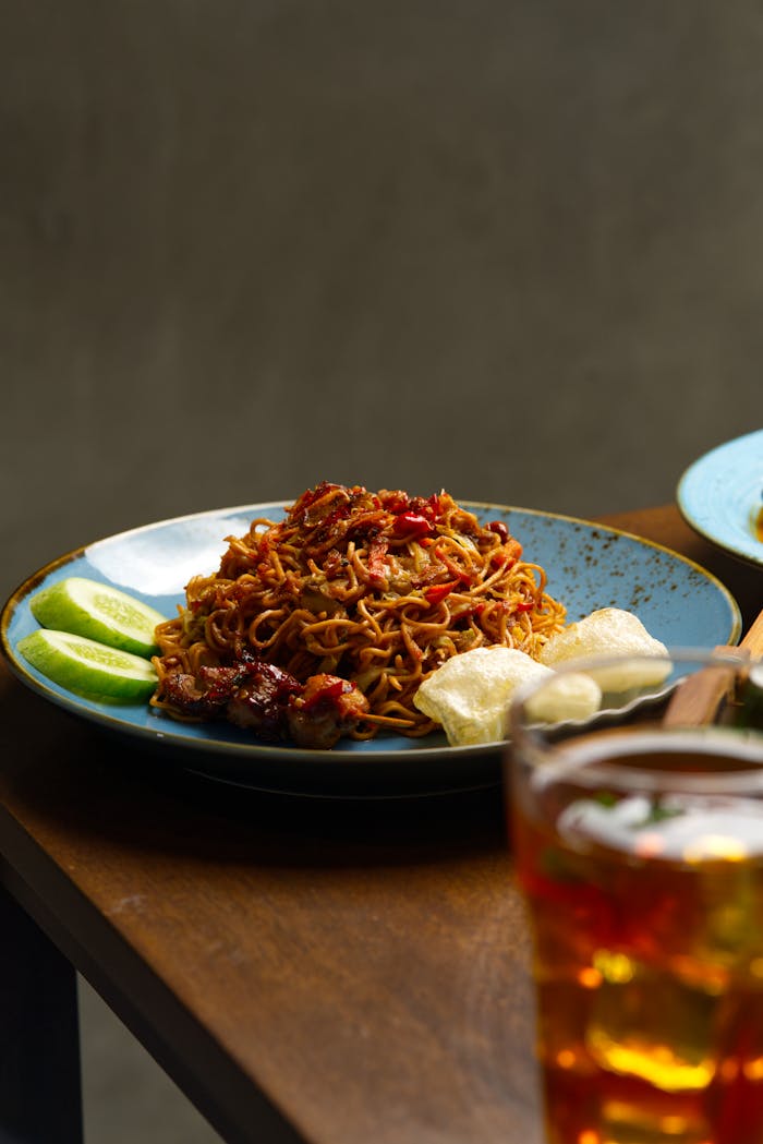 Tasty spicy noodles served with lime slices and iced tea on a wooden table.