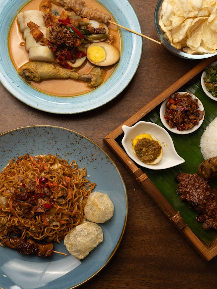 Top view of various Indonesian dishes, including Nasi Padang, noodles, and snacks on a wooden table.