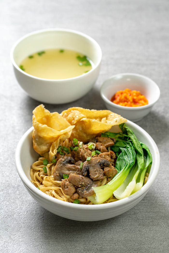 Savor a bowl of Bakmi Ayam Jamur with fresh vegetables and side soup, captured in Bali.