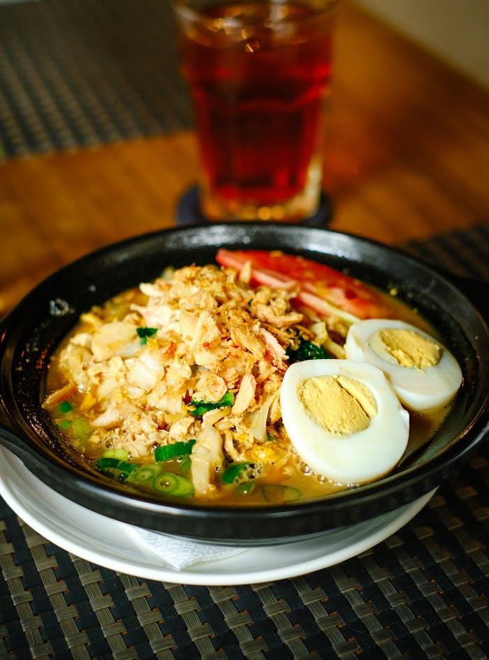 Savory Indonesian noodle soup topped with chicken, fried shallots, boiled egg, and herbs.