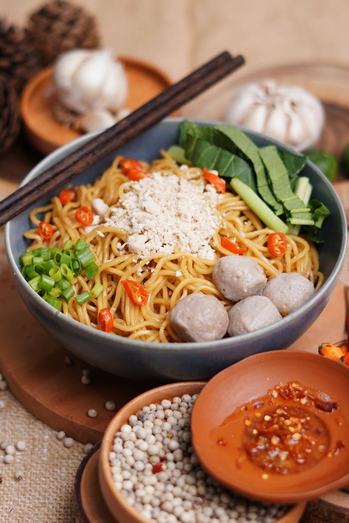 services-img Close-up of Indonesian noodles with meatballs and assorted spices, presented in a rustic setting.